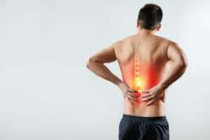 Rear view, the man holds his hands behind his back, pain in the back, pain in the spine, highlighted in red. Light background. The concept of medicine, massage, physiotherapy, health.