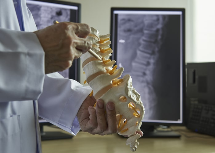 A neurosurgeon pointing at lumbar vertebra model in medical off iStock 1010681402
