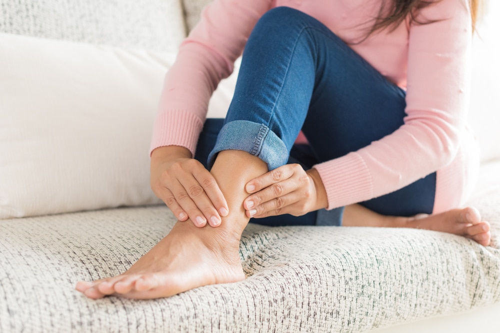 Person holding their ankle and lower leg, suggesting foot drop, nerve pain, or weakness affecting walking.