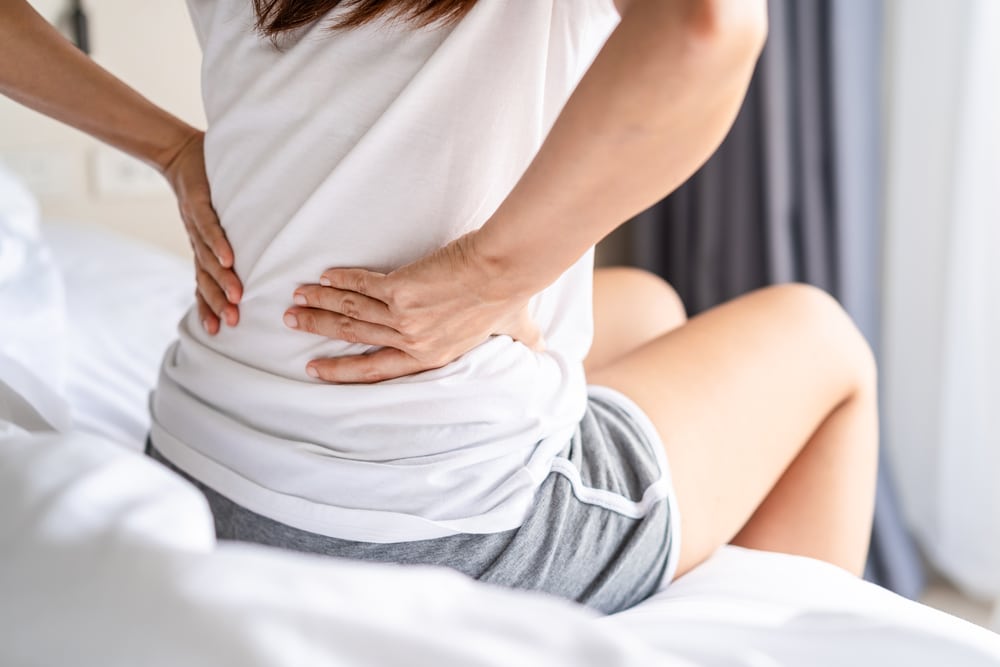 laminectomy 300x200 Person sitting on a bed holding their lower back due to sciatica pain.