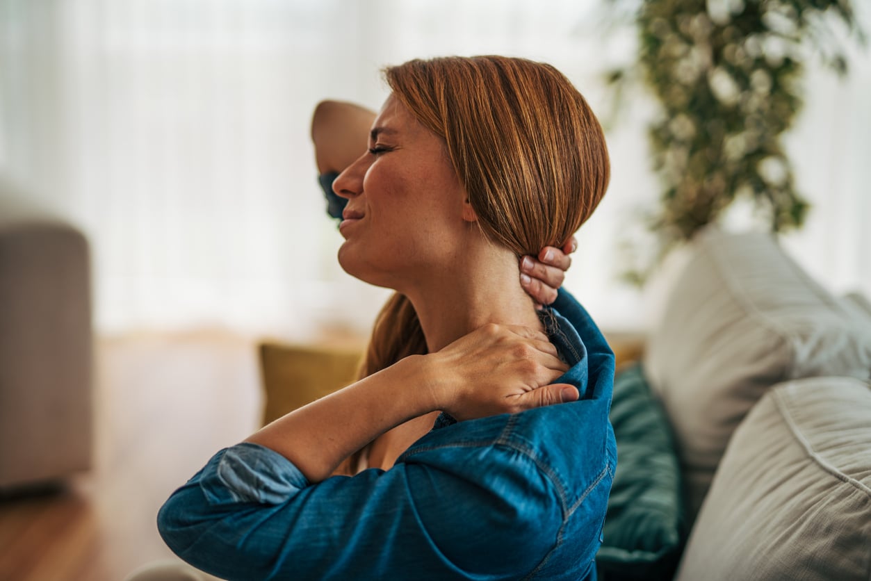 Woman holding her neck and shoulder in discomfort from a possible pinched nerve in the cervical spine.